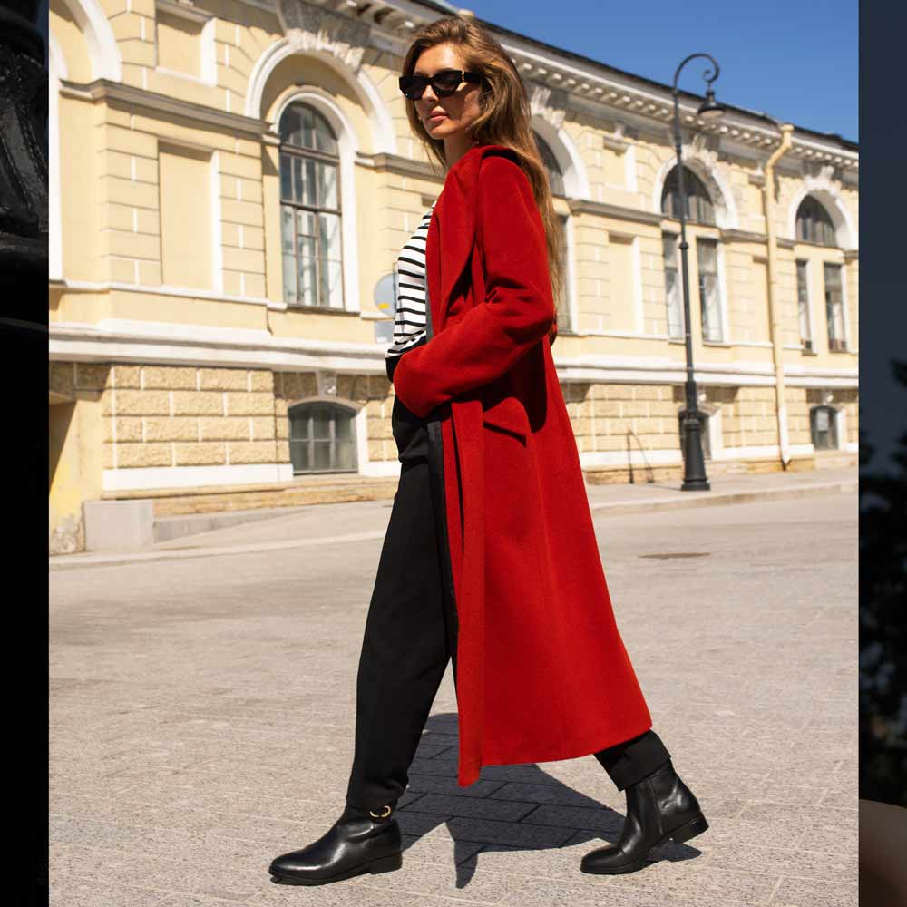 Model walking outdoors wearing black leather ankle boots with a gold buckle