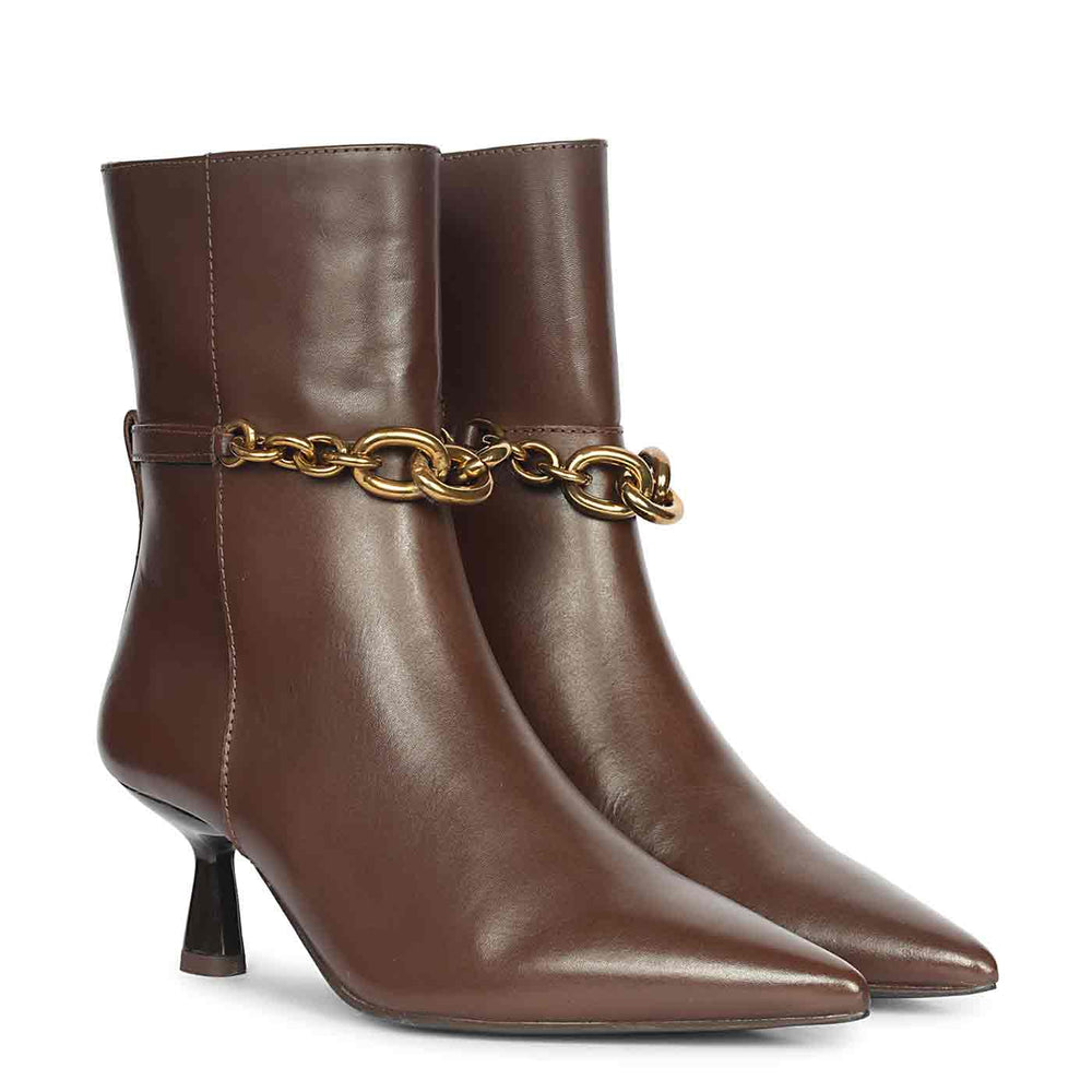 Pair of brown leather ankle boots with pointed toes and gold chain embellishment shown from an angled front view