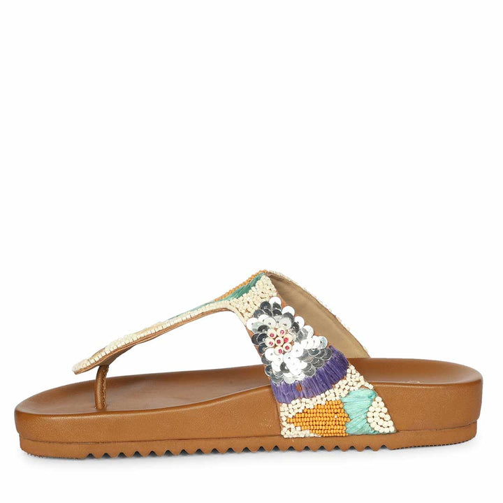 Tan sandal with a decorative strap featuring flowers and beads on a white background