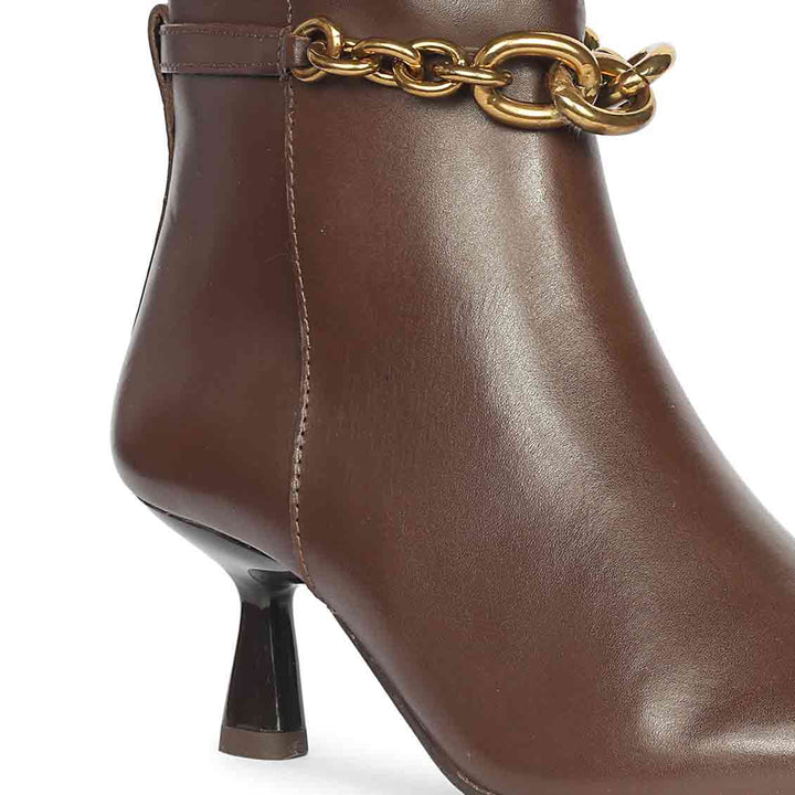 Close-up side view of brown leather ankle boot highlighting the gold chain embellishment