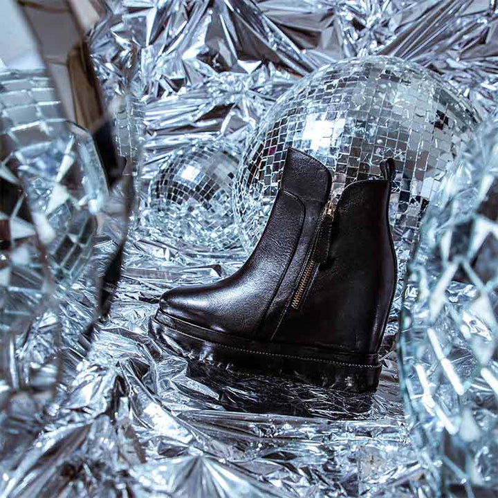 Black leather wedge ankle boots for women, styled on a festive background