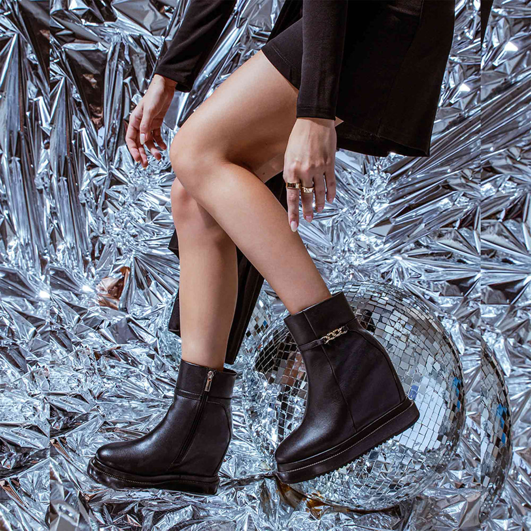 Model wearing ladies black leather wedge ankle boots, styled on a festive background