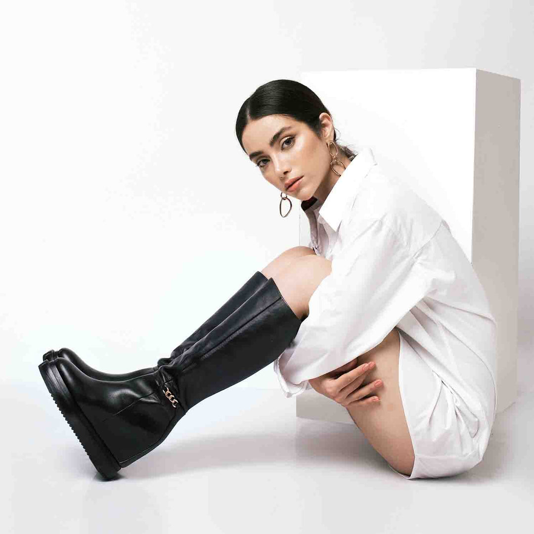 Model wearing ladies black leather wedge knee-high boots, styled look