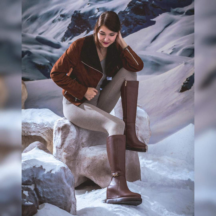 Model wearing ladies tan leather wedge knee-high boots in a winter setting