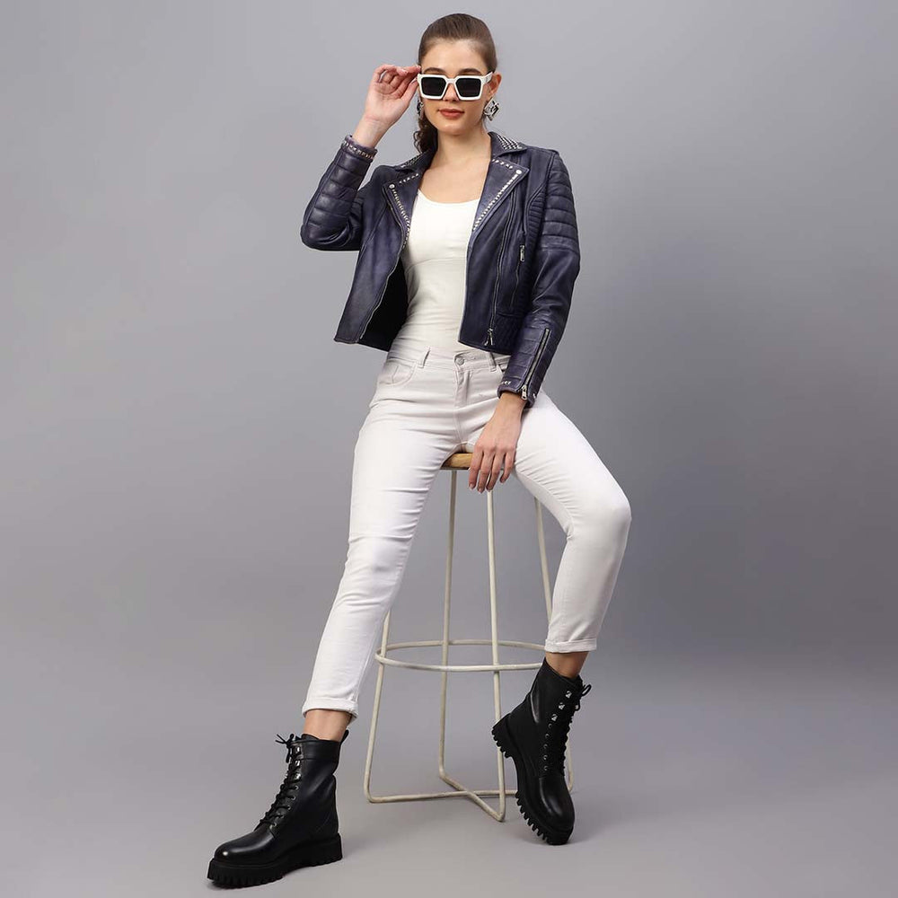 Women's blue leather biker jacket UK by Saint Brielle, styled seated lifestyle shot