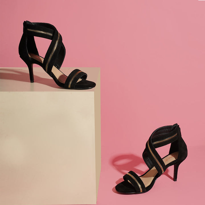 Saint Delilah black suede stiletto sandals in a styled editorial shot with gold zip trim detail