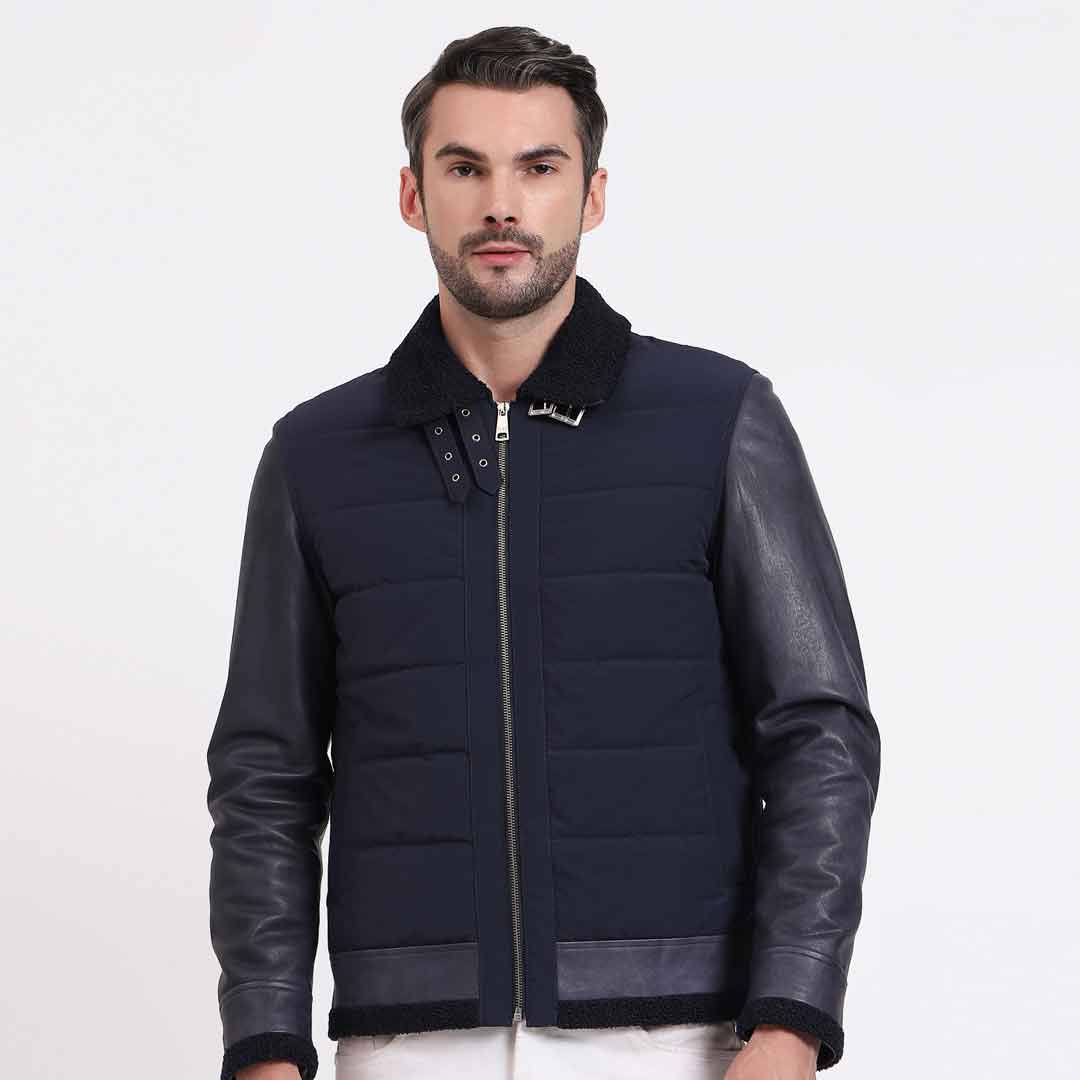 Man wearing an open navy quilted jacket with black leather sleeves.