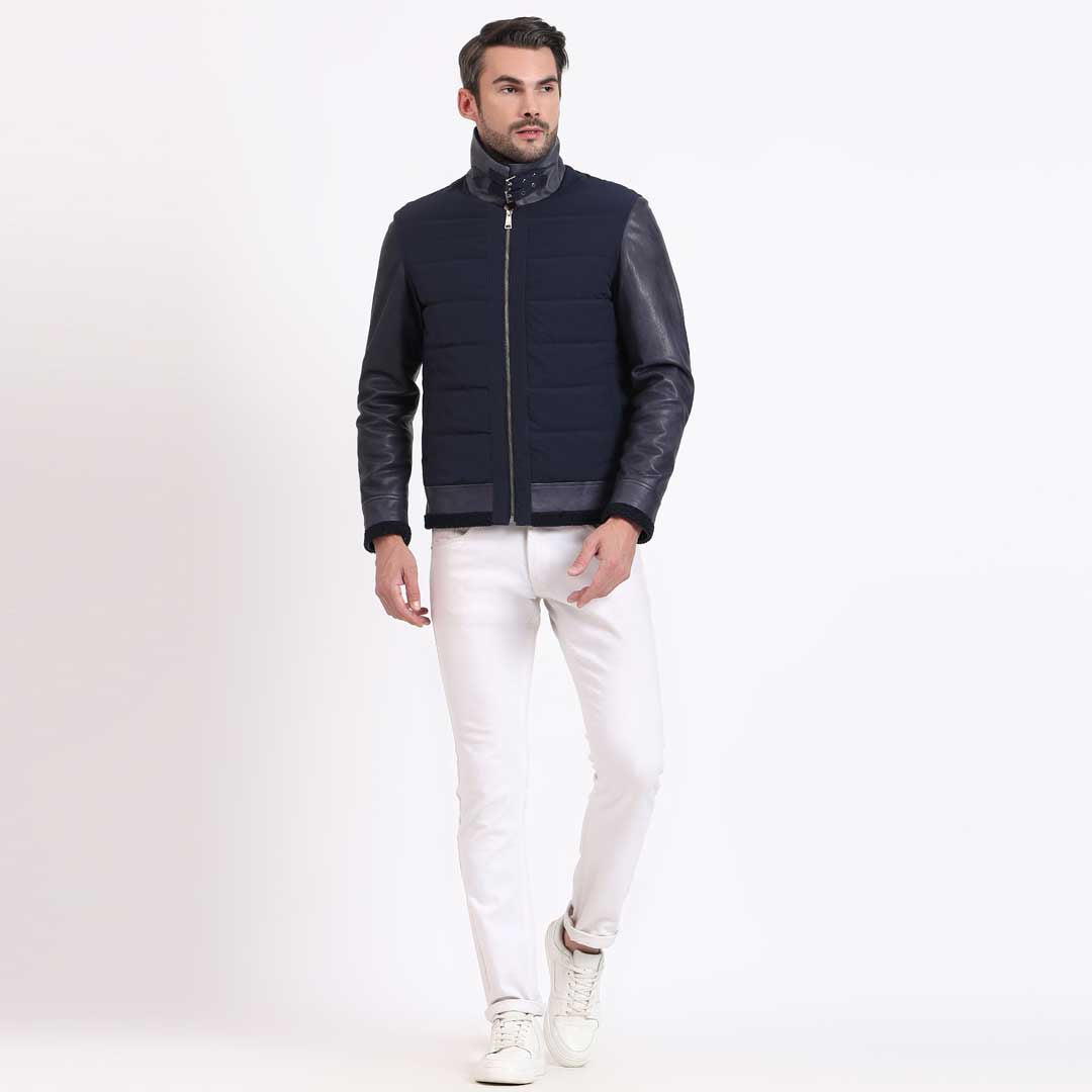 Full-length shot of a man wearing a navy quilted jacket with black leather sleeves.