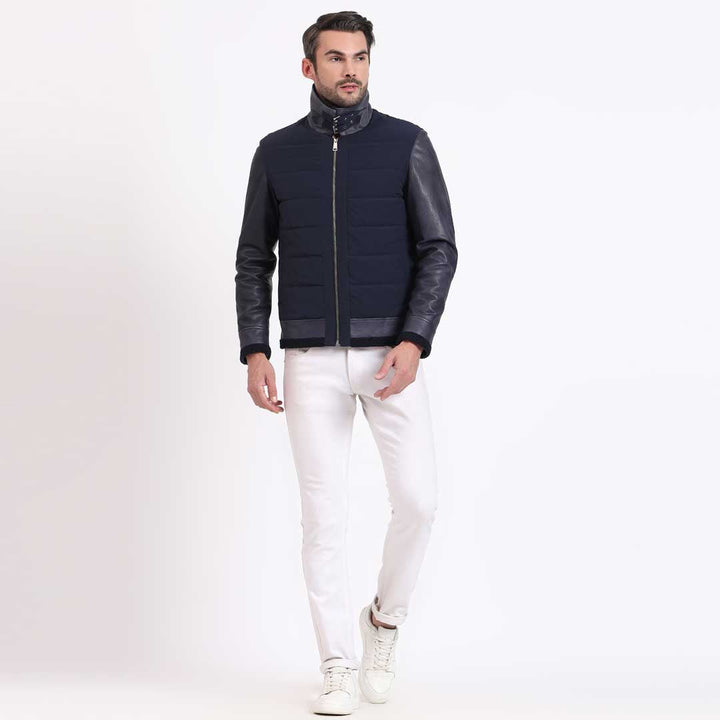 Full-length shot of a man wearing a navy quilted jacket with black leather sleeves.