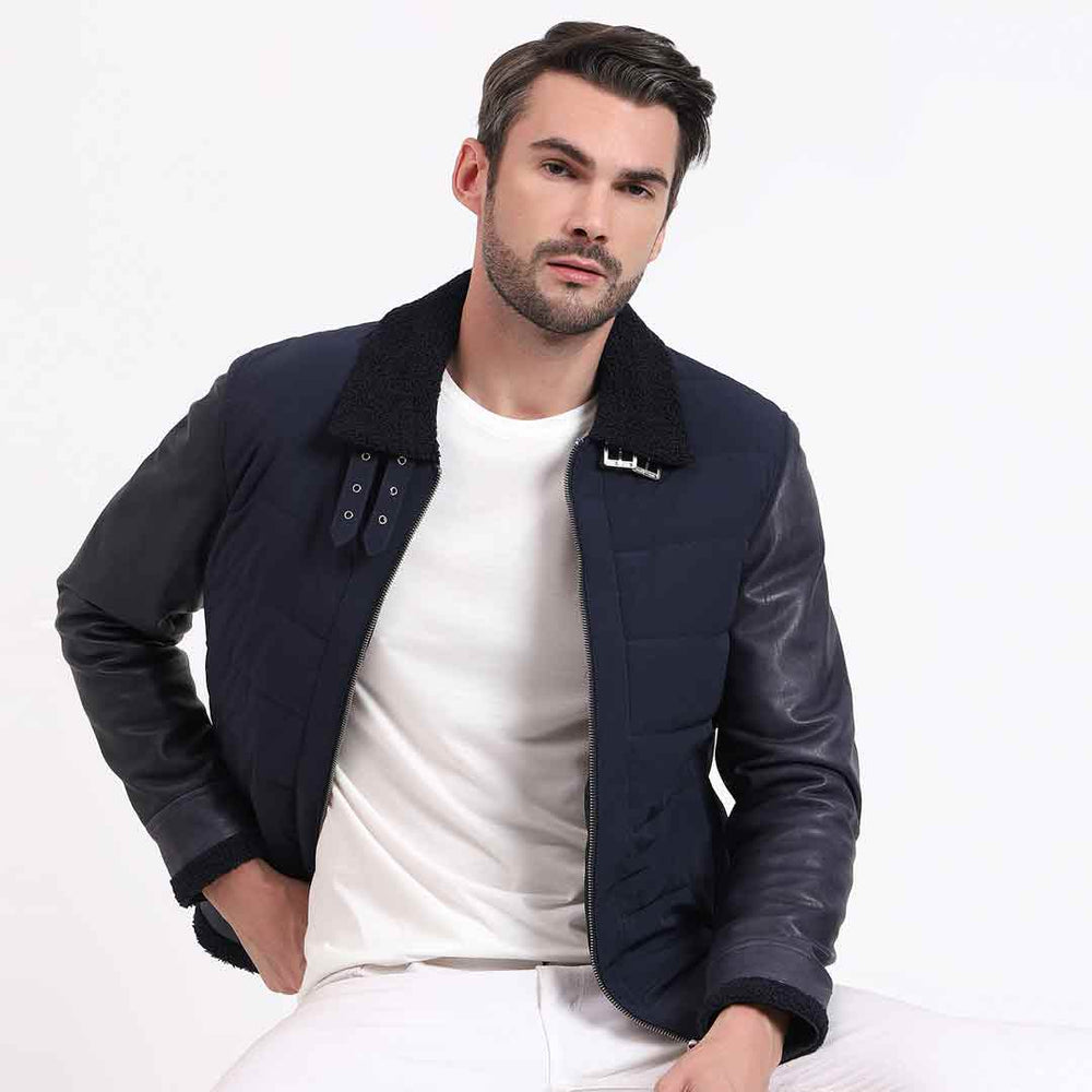 Man wearing a zipped-up navy quilted jacket with black leather sleeves.