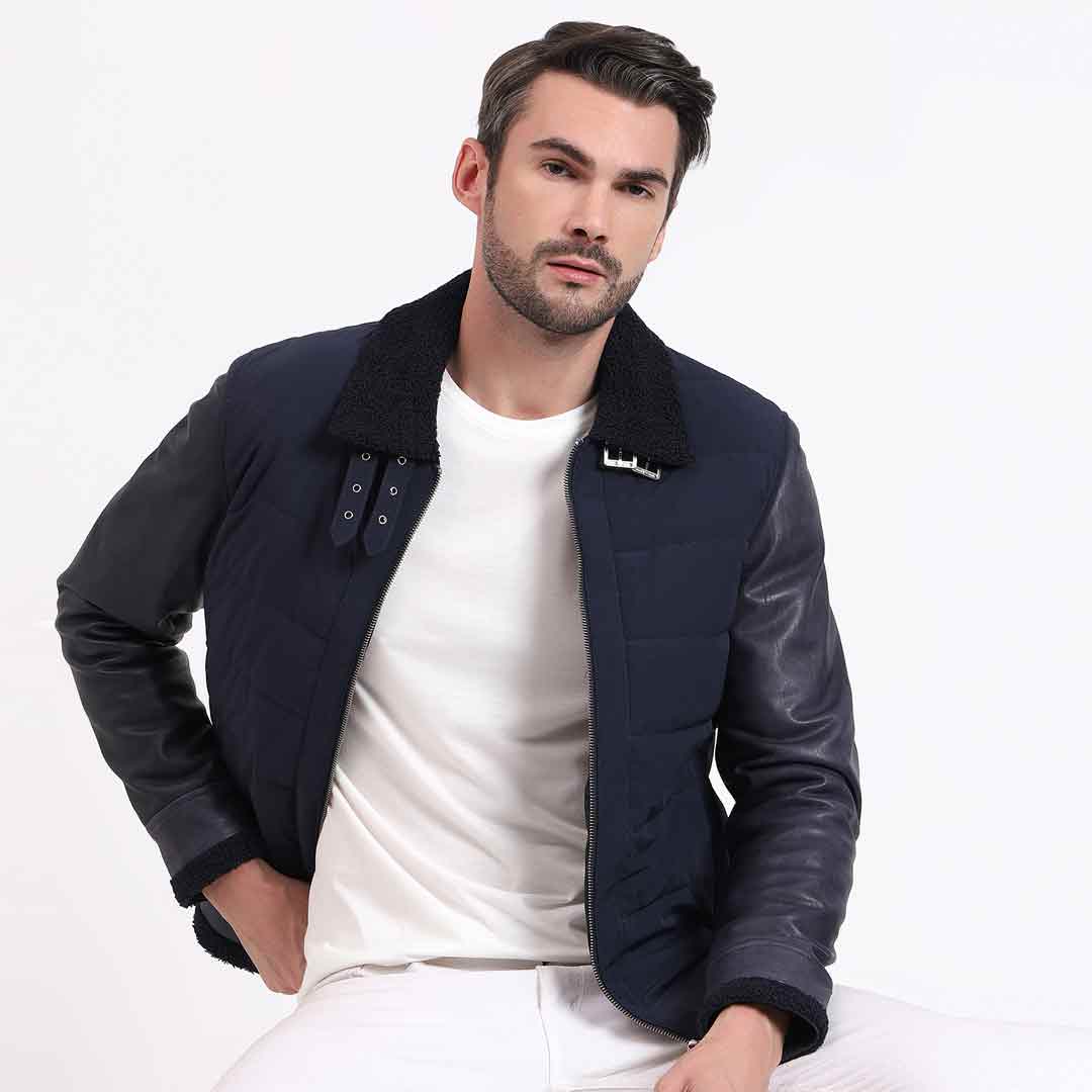 Man wearing a zipped-up navy quilted jacket with black leather sleeves.