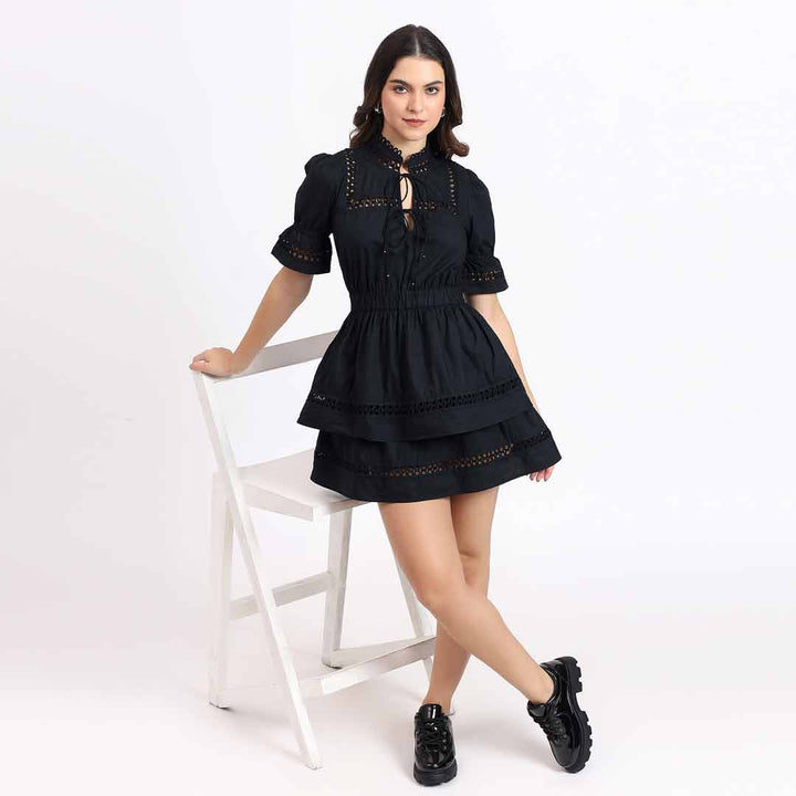 Women's black lace-trim tiered short dress by Saint Gianna, seated lifestyle view.