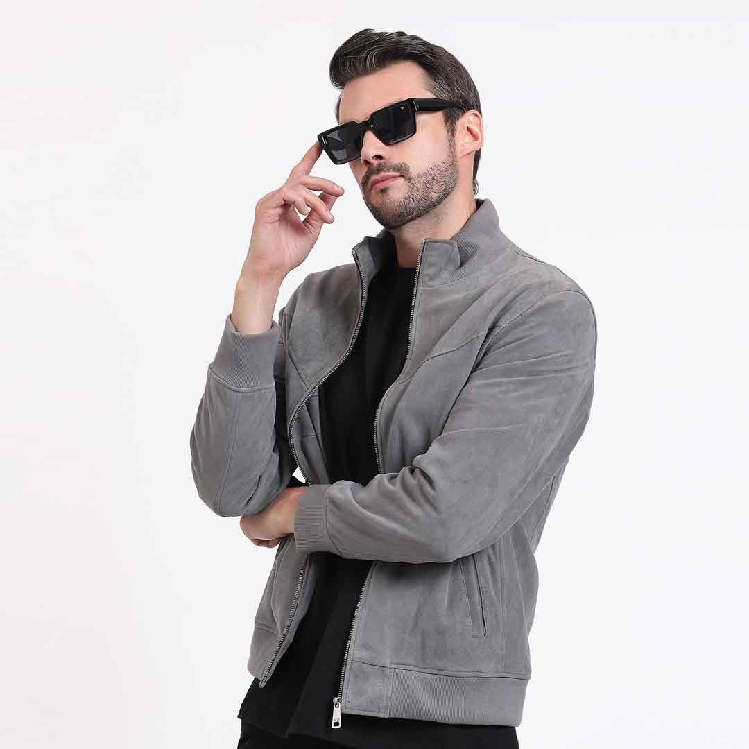 Man wearing a grey jacket, arms crossed, side pose with sunglasses.