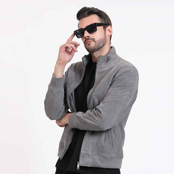 Man wearing a grey jacket, arms crossed, side pose with sunglasses.