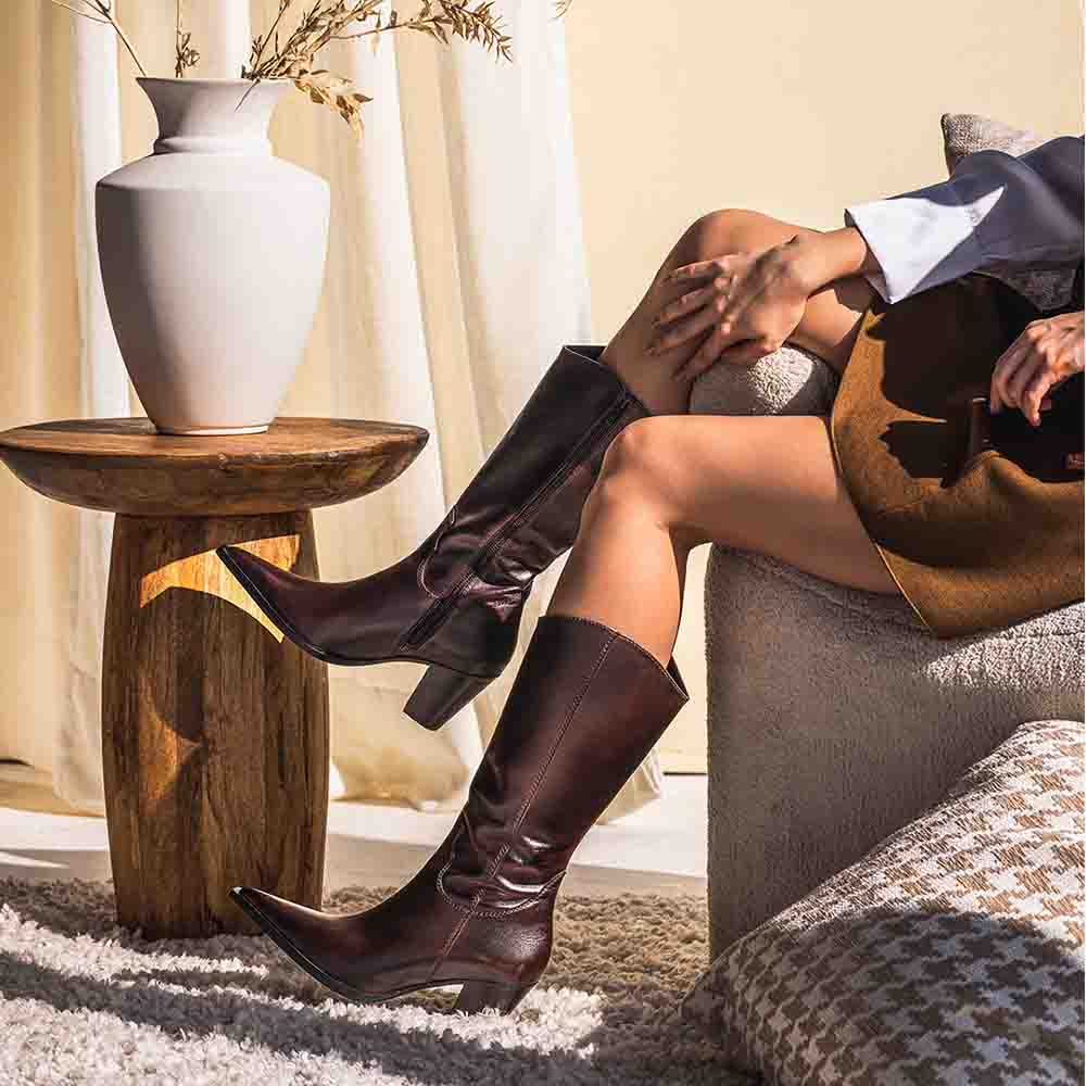 Women's brown leather knee high boots by Saint Prune, styled seated indoors, lifestyle view