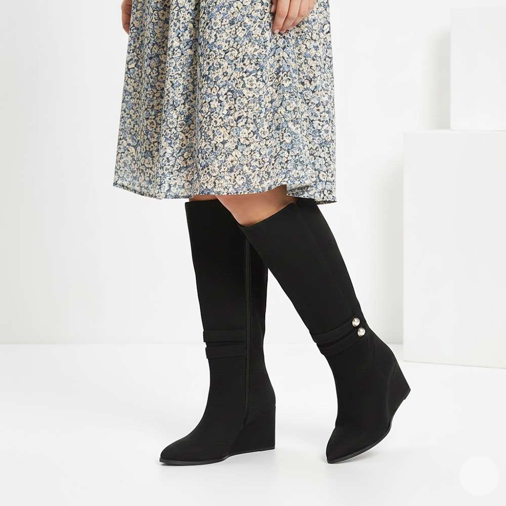 Women's black suede wedge knee high boots by Saint Rosabel, styled with a floral dress, lifestyle view
