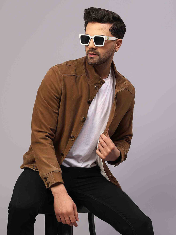 Man sitting on a stool wearing an open tan suede jacket over a white t-shirt.