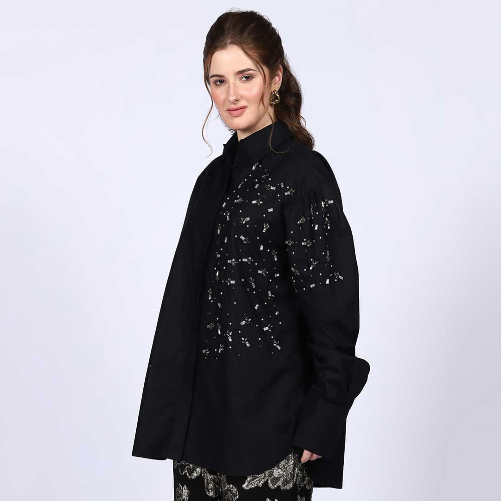 Side view of a woman wearing a black cotton shirt with rhinestone detailing.