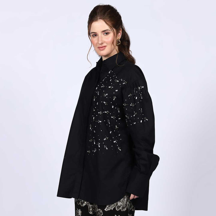 Side view of a woman wearing a black cotton shirt with rhinestone detailing.