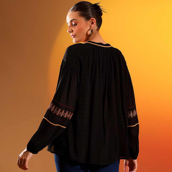 Back view of a woman wearing a black viscose top with embroidered sleeve trim.