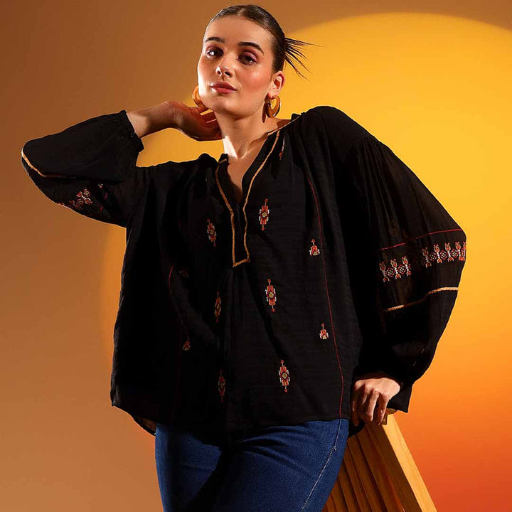 Woman wearing a black viscose top with scattered embroidered diamond motifs and balloon sleeves.