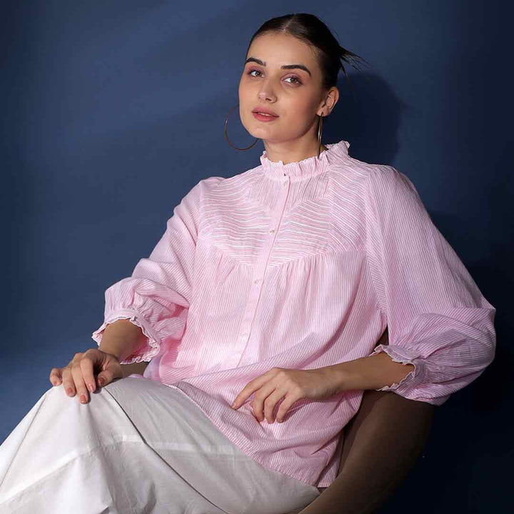Woman seated, wearing a blush yarn-dyed striped cotton top.