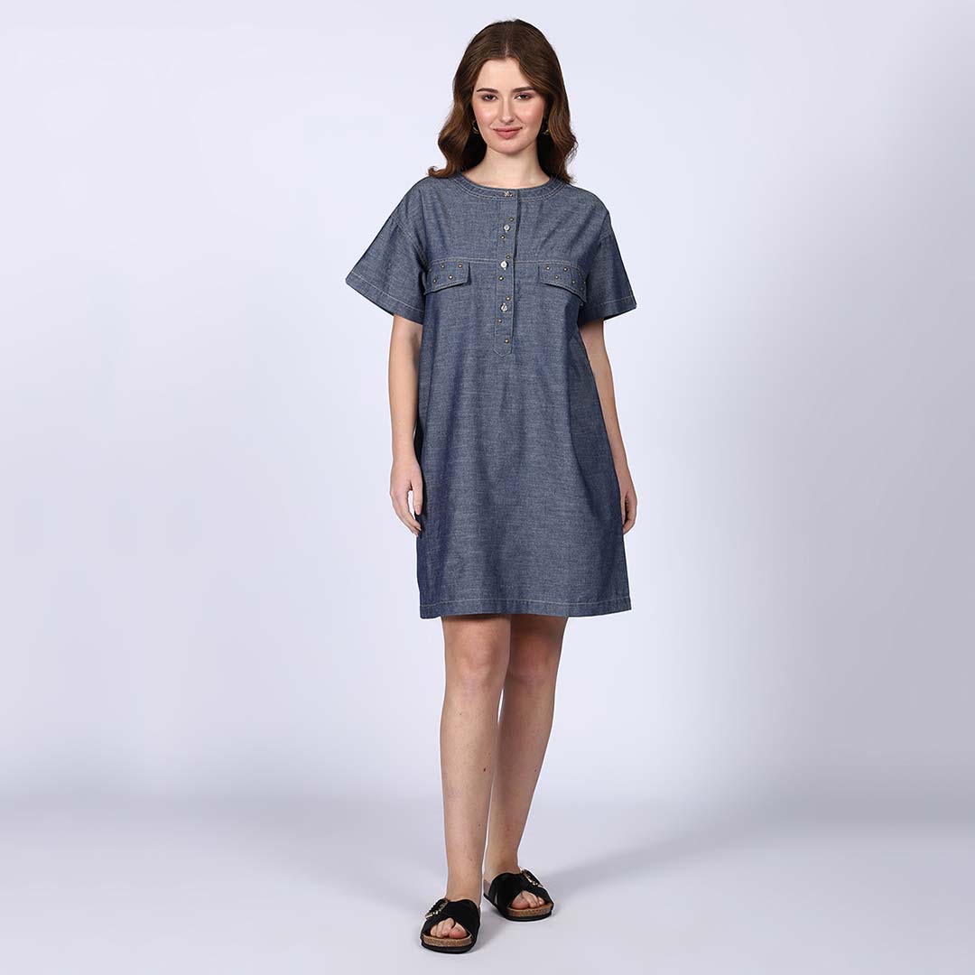 Woman wearing a grey chambray short dress with a button placket and chest pockets.