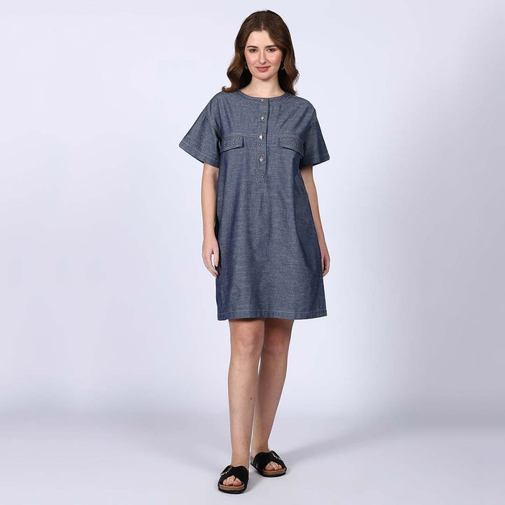 Woman wearing a grey chambray short dress with a button placket and chest pockets.