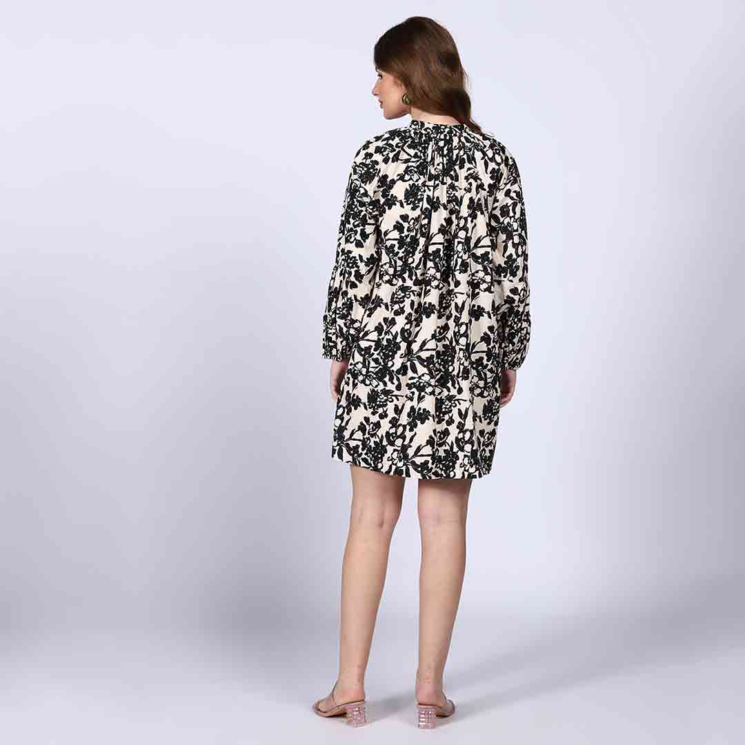Back view of a woman wearing a black floral print dress on an ivory background.