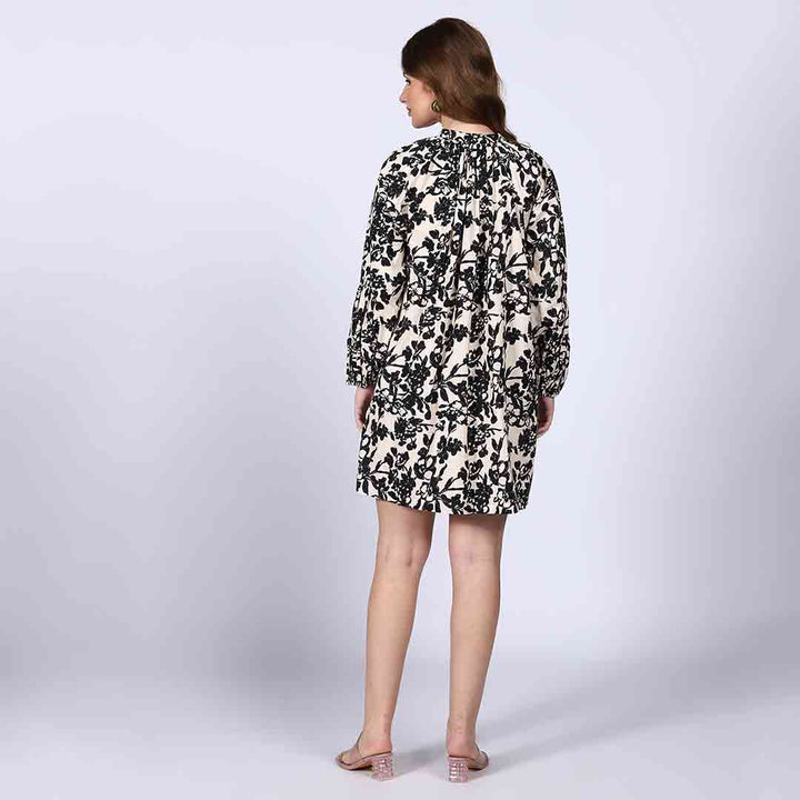 Back view of a woman wearing a black floral print dress on an ivory background.