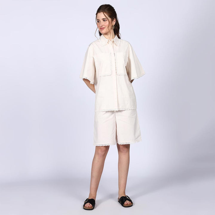 Woman wearing a solid ivory cotton poplin co-ord set with crochet-trimmed bell sleeves.