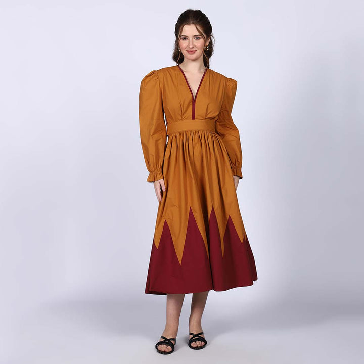 Woman wearing a mustard and burgundy colour-block midi dress with a zigzag hemline.