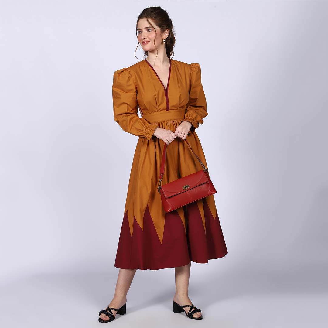 Woman wearing a mustard V-neck dress, carrying a red handbag.