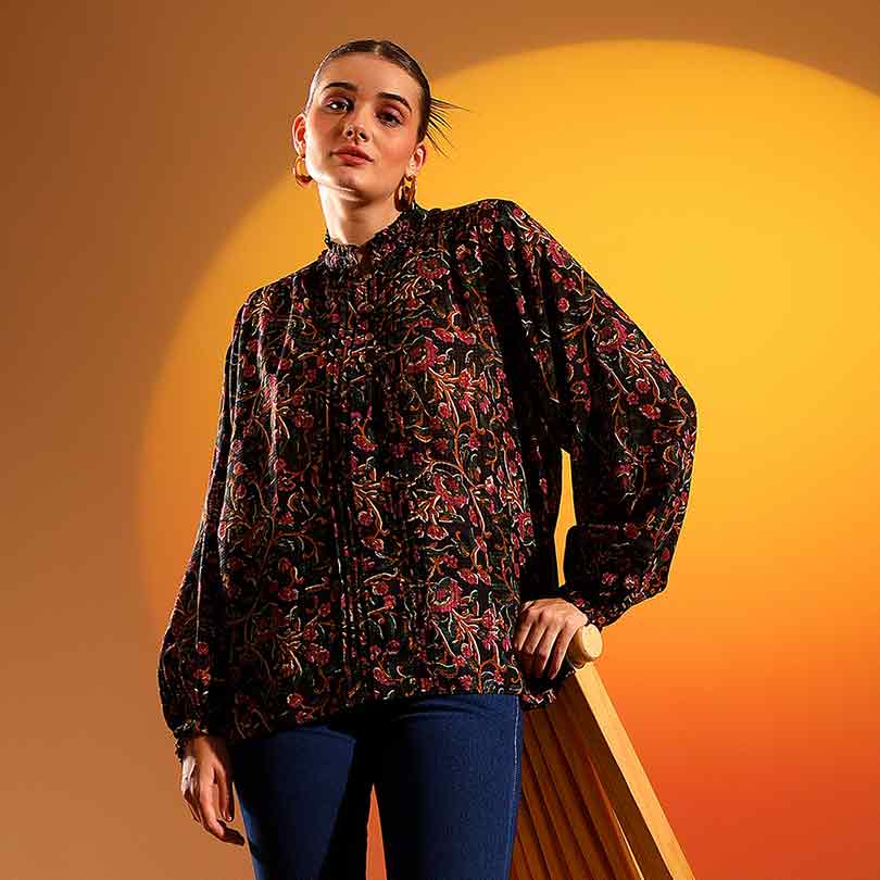 Woman wearing an onyx-black top with a multicolour floral print and balloon sleeves.
