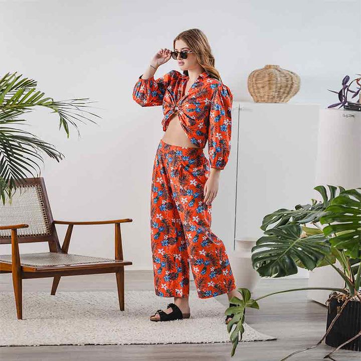 Woman wearing an orange floral tropical-print crop top and wide-leg trousers co-ord set.