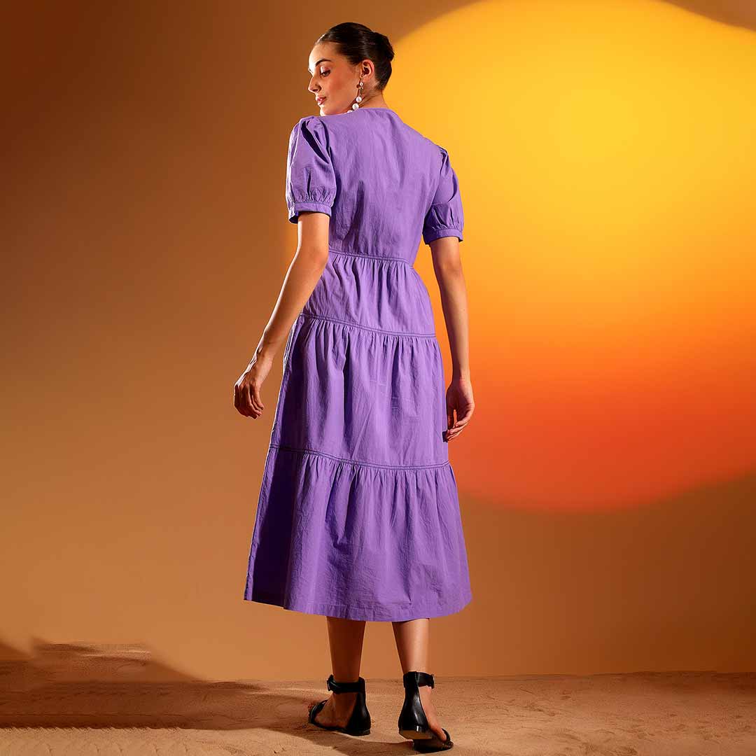 Back view of a woman wearing a purple/iris cotton tiered midi dress.