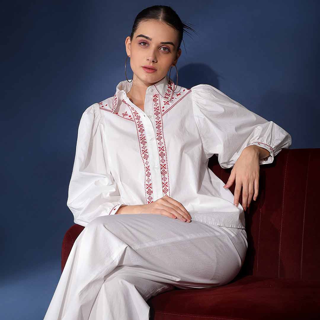 Full-length shot of a woman wearing a white embroidered cotton shirt and trousers.