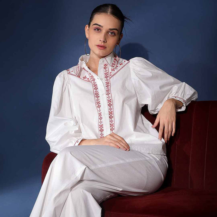 Full-length shot of a woman wearing a white embroidered cotton shirt and trousers.