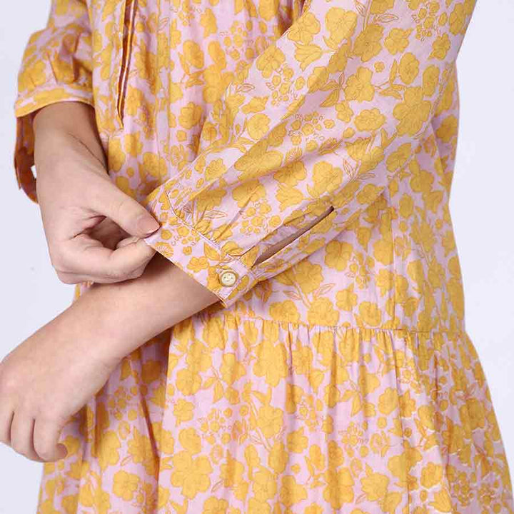 Full-length shot of a woman wearing a yellow multicolour tiered midi dress, showing calf-length hem.